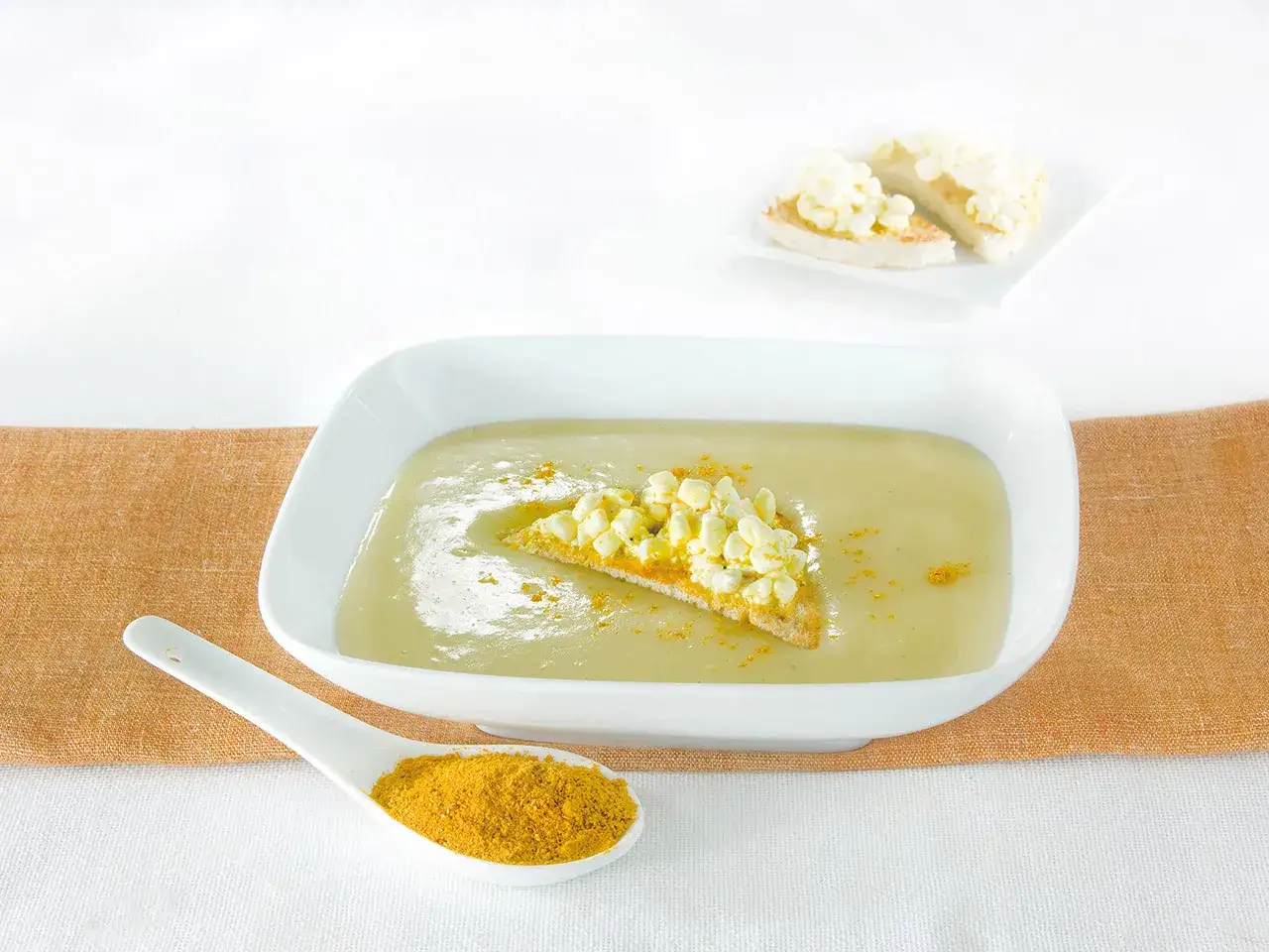 Una cremosa crema di patate servita in una ciotola bianca, guarnita con crostini e una spolverata di curcuma.