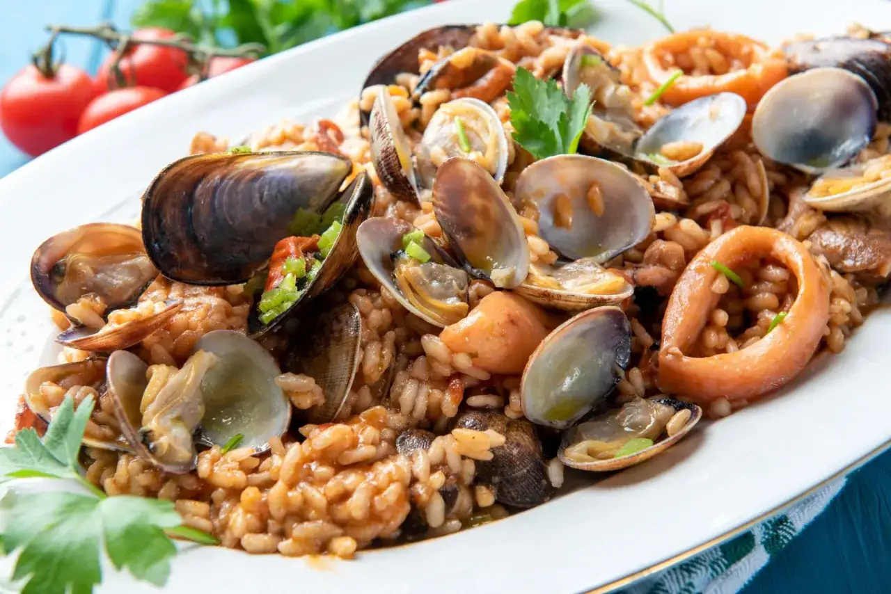 Un invitante risotto allo scoglio, ricco di cozze, vongole e anelli di calamaro, guarnito con prezzemolo fresco.