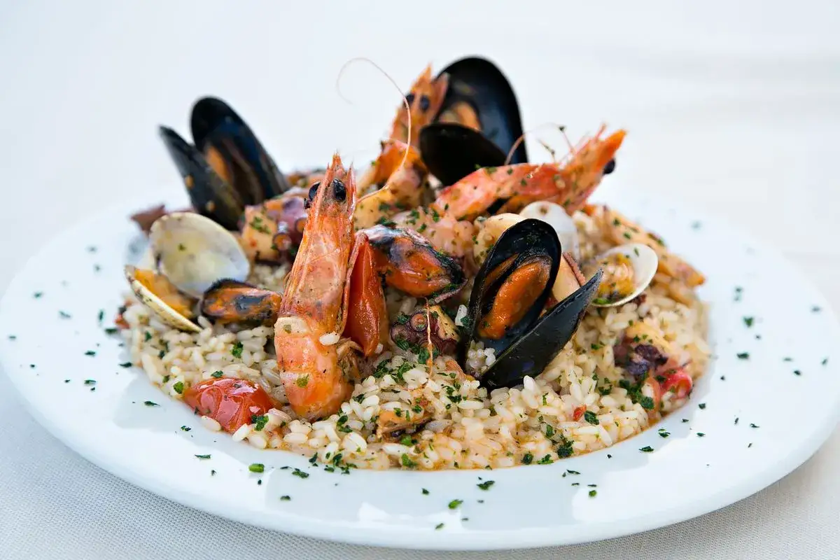 Un invitante risotto allo scoglio, ricco di gamberi, cozze, vongole e polpo, guarnito con prezzemolo fresco e pomodorini.