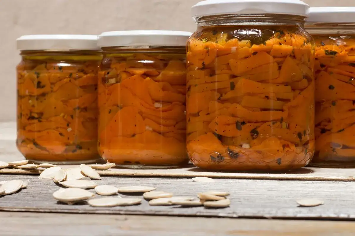 Barattoli di zucca sott'olio in agrodolce, con semi di zucca sparsi sul tavolo di legno.