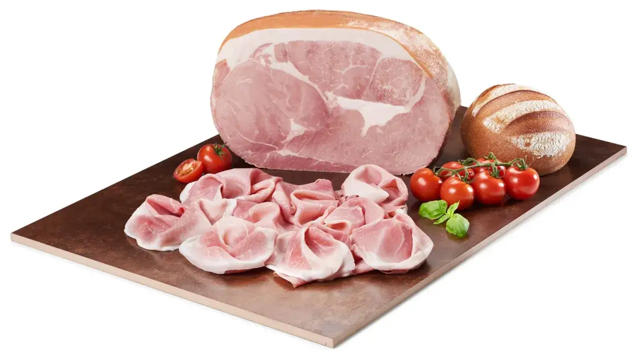 Un intero cotto prosciutto, fette sottili, pomodorini e pane rustico su un tagliere di rame.