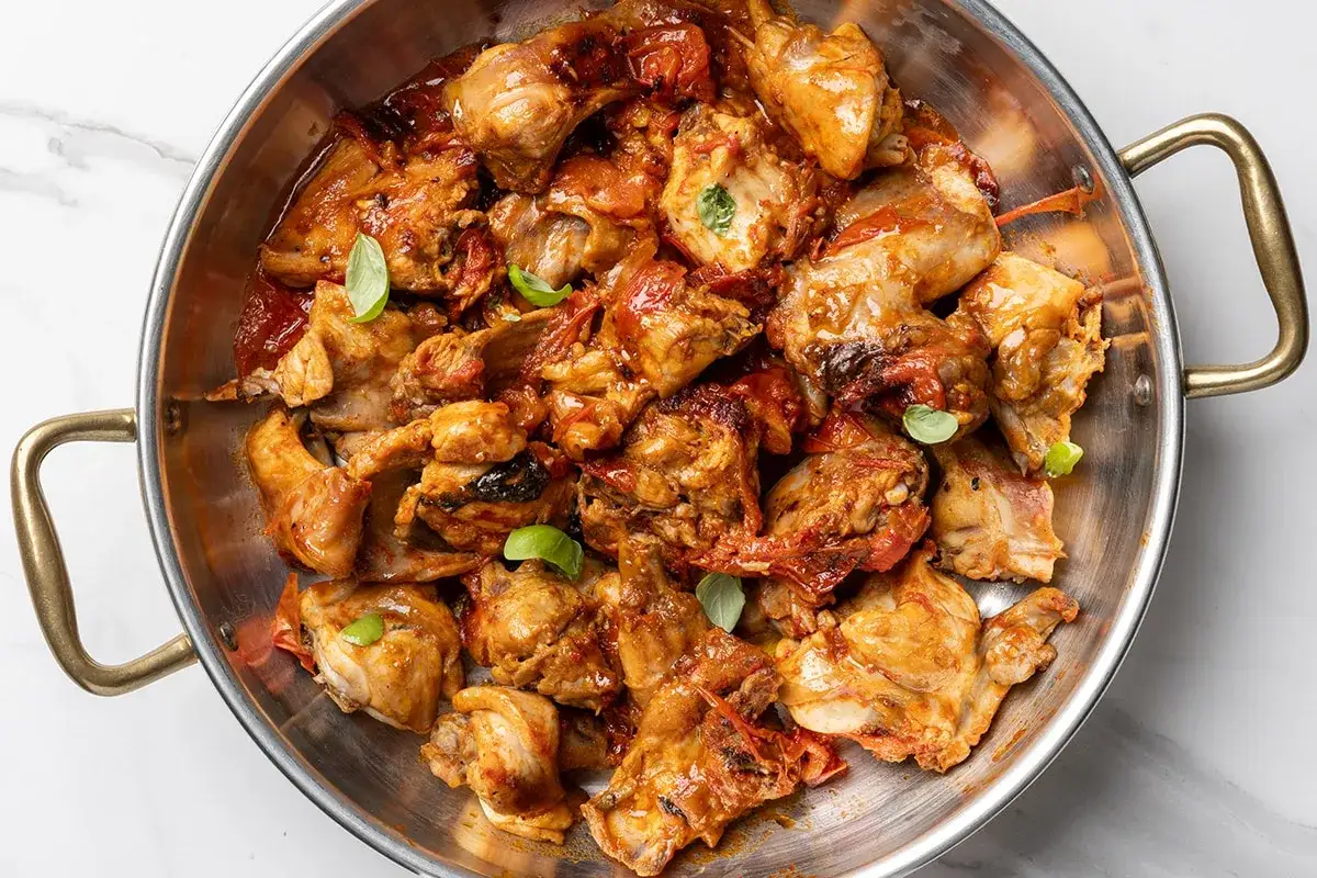Un saporito coniglio all'ischitana, cotto in padella con pomodoro e basilico, pronto per essere gustato.
