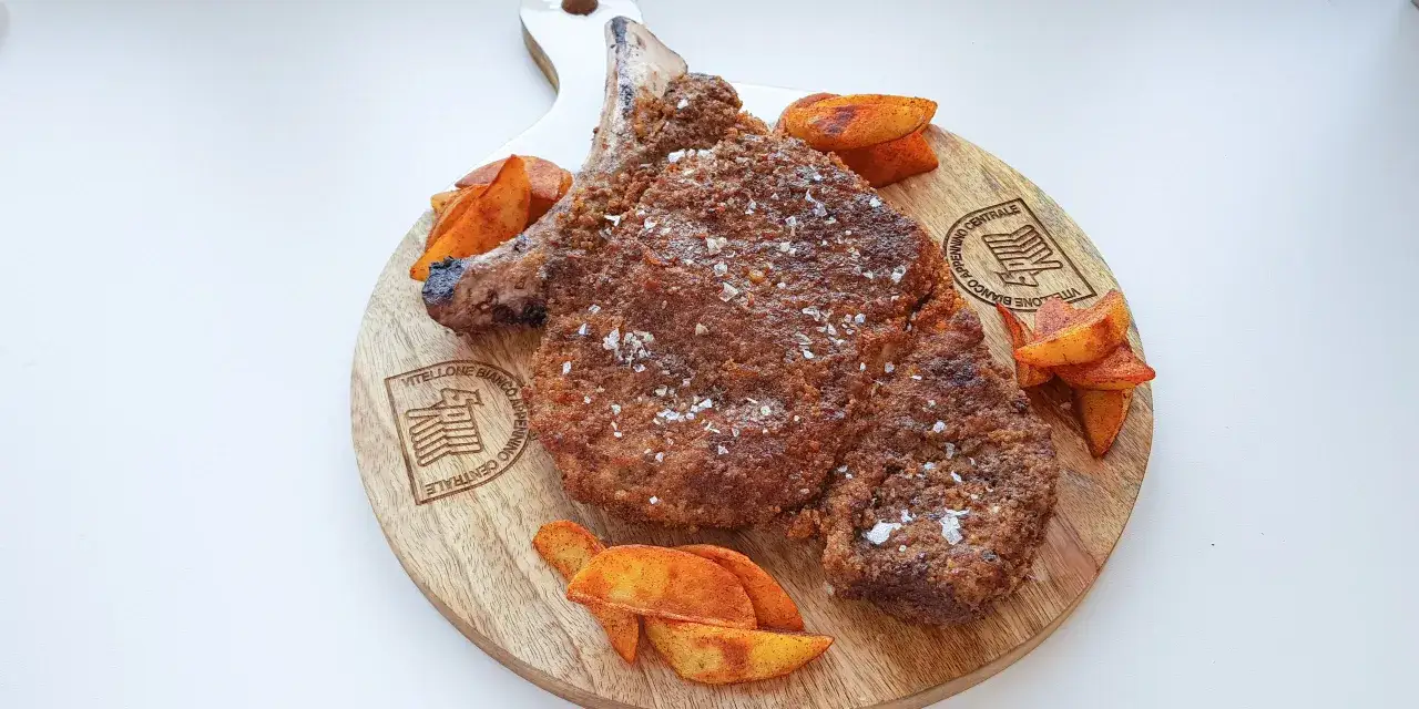 Bistecca impanata con patate speziate su tagliere di legno. Un esempio di come il manzo magro cos'è, gustoso e croccante.