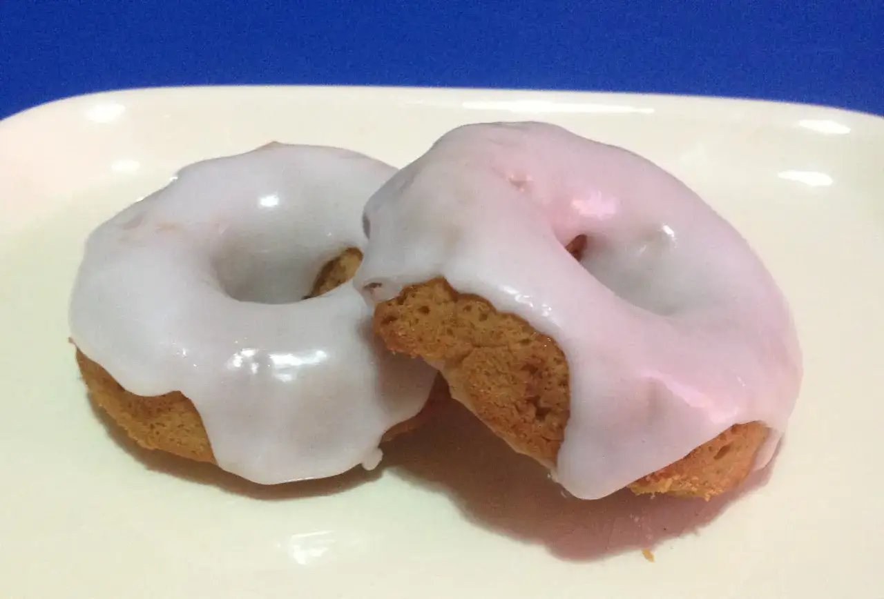 Due ciambelle con glassa di zucchero bianca e lucida, perfette per chi vuole imparare come fare la glassa di zucchero.