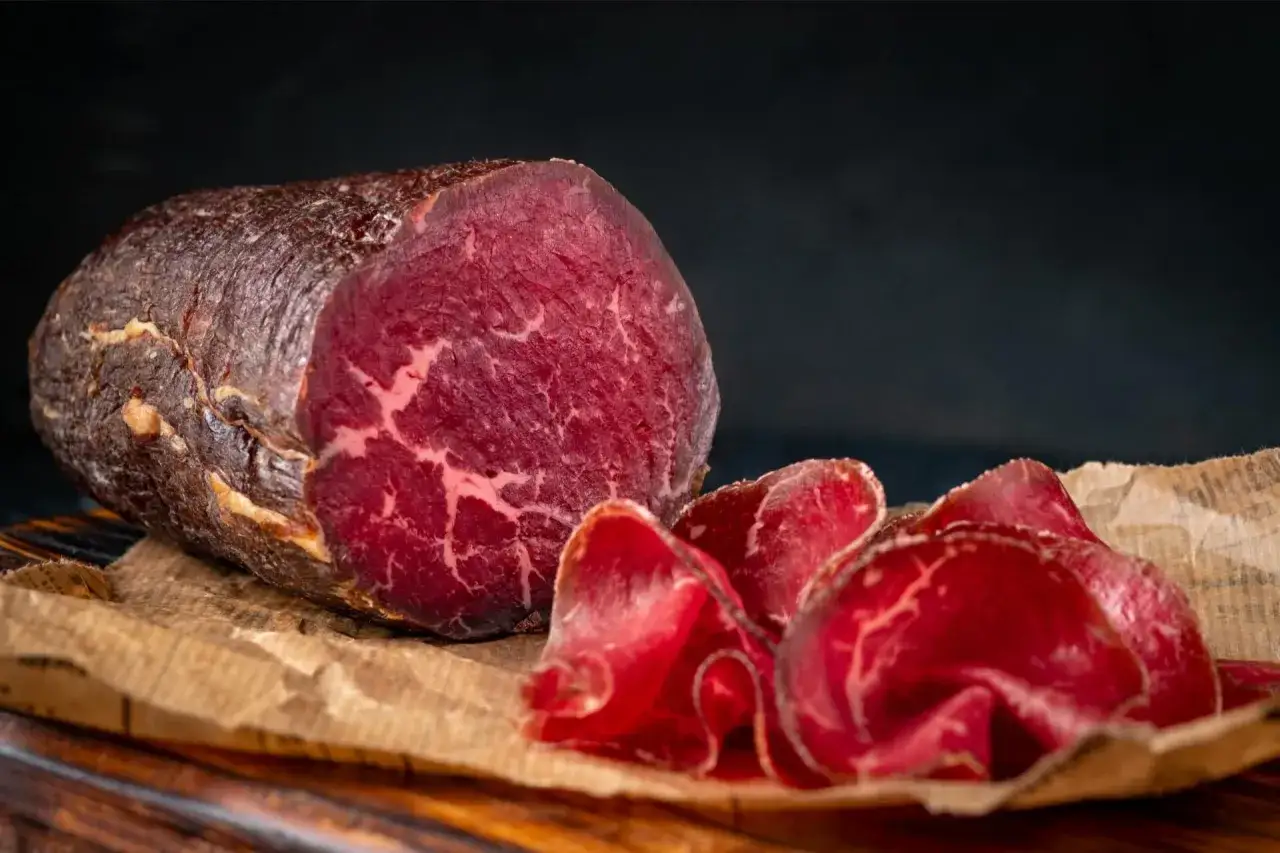 Un pezzo intero e fette sottili di bresaola, con la sua carne rossa e marezzata, evidenziano la differenza tra bresaola e punta d'anca.