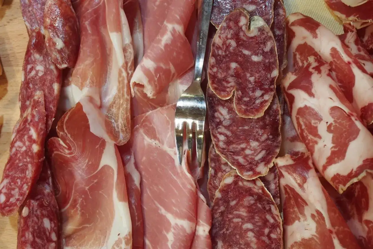 Assortimento di salumi non insaccati: fette di prosciutto crudo, coppa e salami stagionati, con una forchetta al centro.
