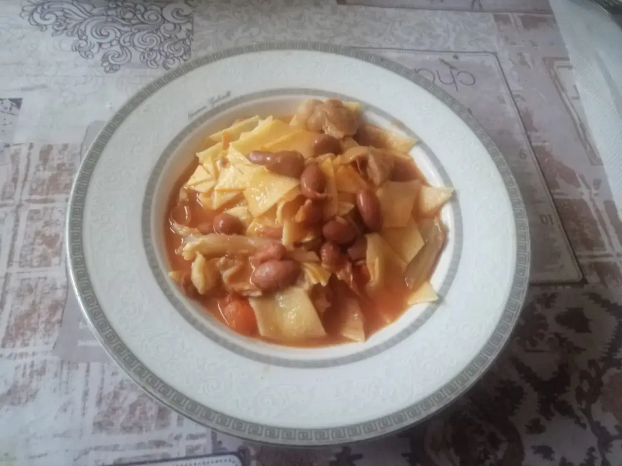 Piatto di pasta fresca con fagioli borlotti e pezzi di zampone in un sugo rosso.