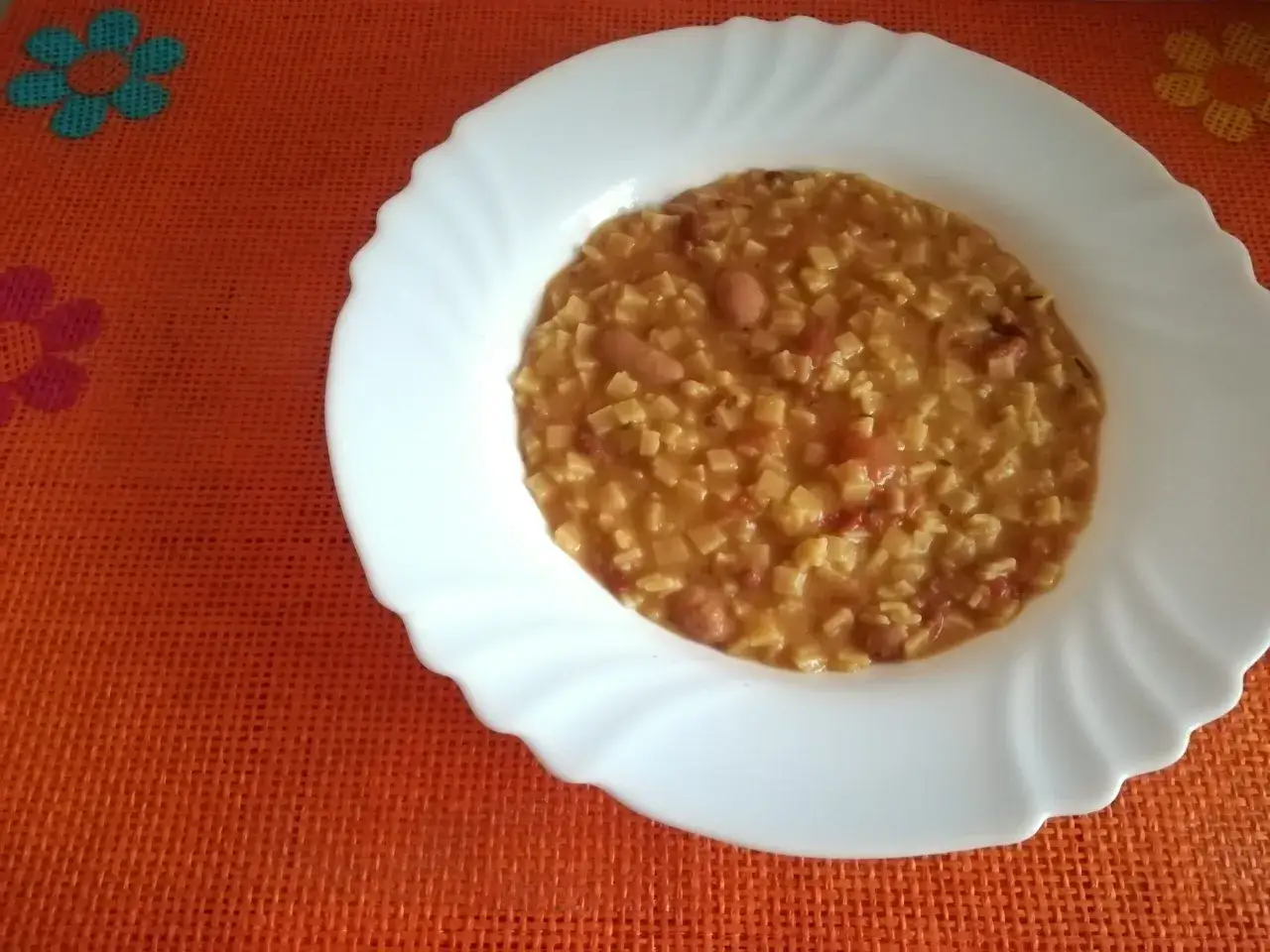 Un piatto bianco con pasta e fagioli saporita su una tovaglietta arancione con fiori.