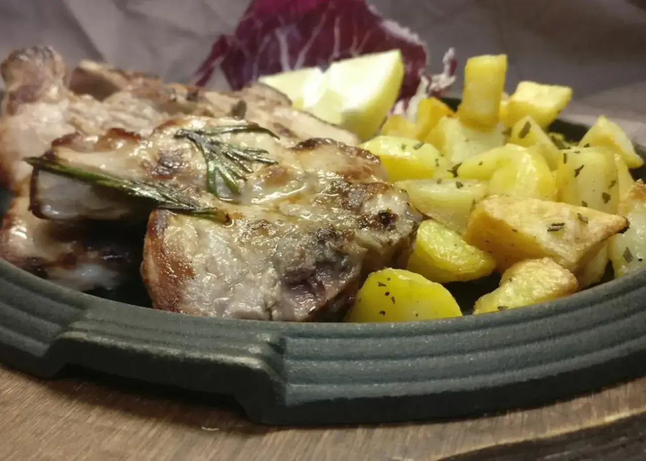 Succulente costine di maiale al forno con patate dorate, profumate al rosmarino, servite con spicchi di limone e radicchio.