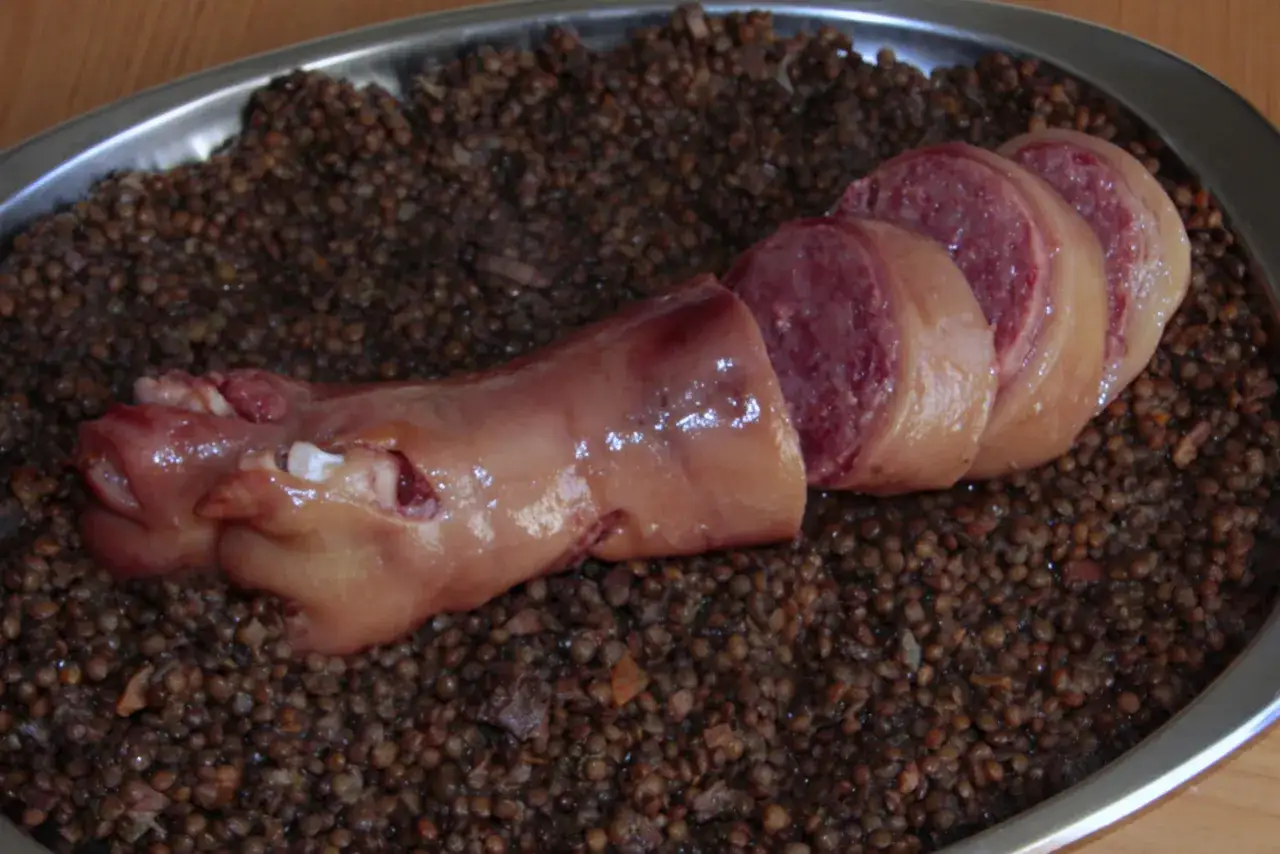 Piatto di lenticchie con cotechino, un salume di carne di maiale, tagliato a fette.