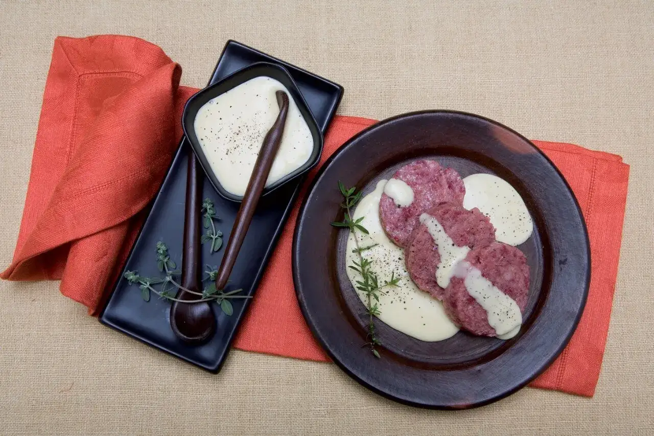 Fette di cotechino su un piatto scuro, accompagnate da una cremosa salsa. Un'elegante presentazione per un piatto tradizionale.