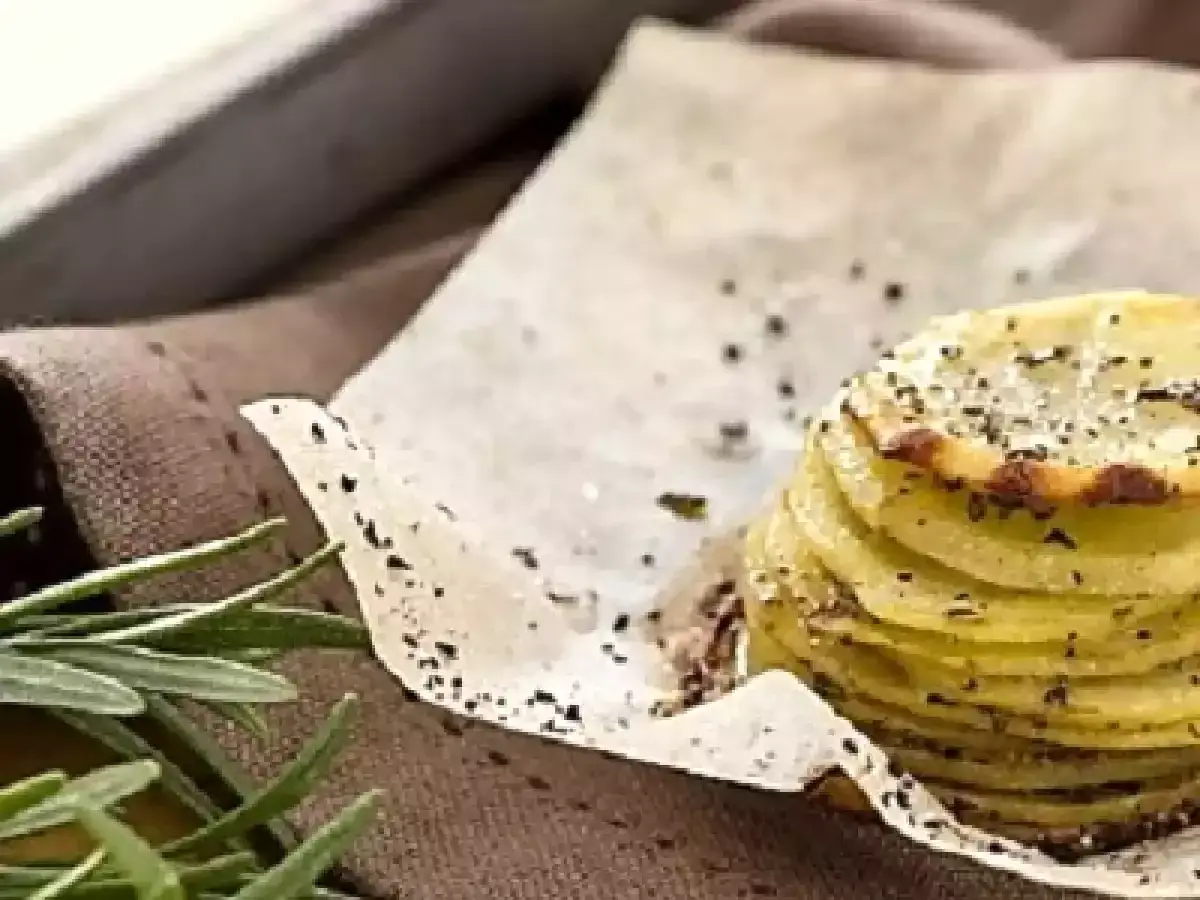 Deliziosa torretta di patate, condita con sale e pepe, su carta forno, con rosmarino fresco a lato.