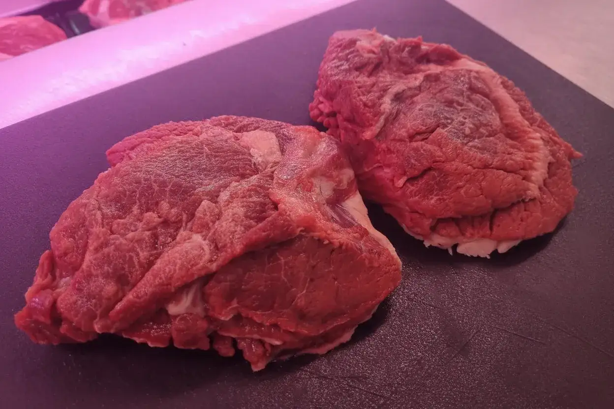 Due pezzi di guancia di manzo cruda, ricchi di tessuto connettivo, pronti per una lunga e saporita cottura.