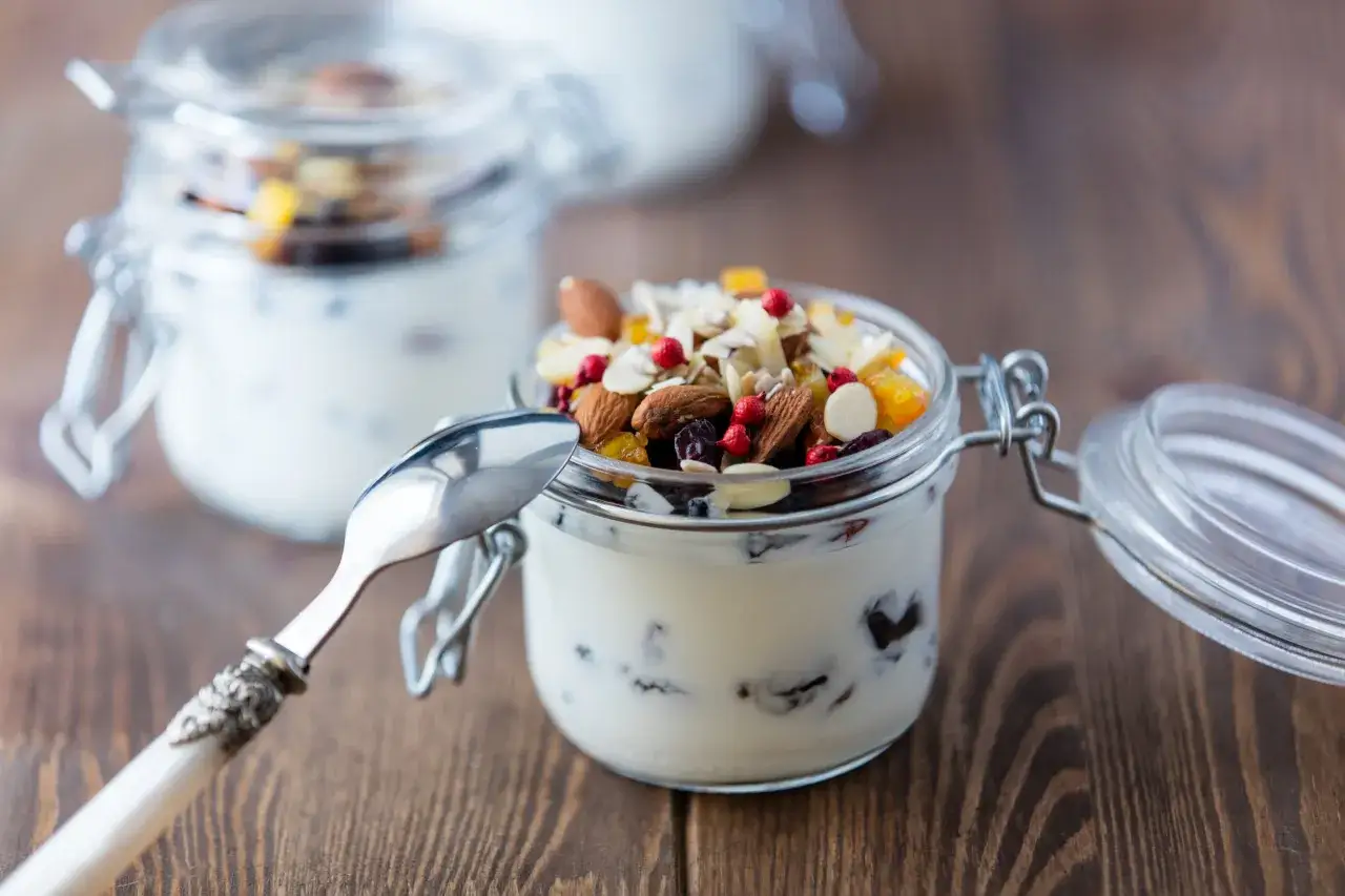 Un vasetto di yogurt con frutta secca e mandorle, pronto per una colazione sana e gustosa.