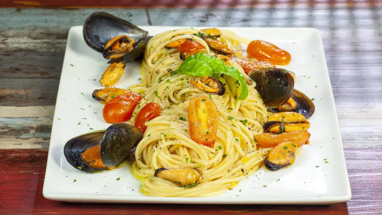 Spaghetti con le cozze e pomodorini, un piatto di pasta profumato e saporito, guarnito con basilico fresco.