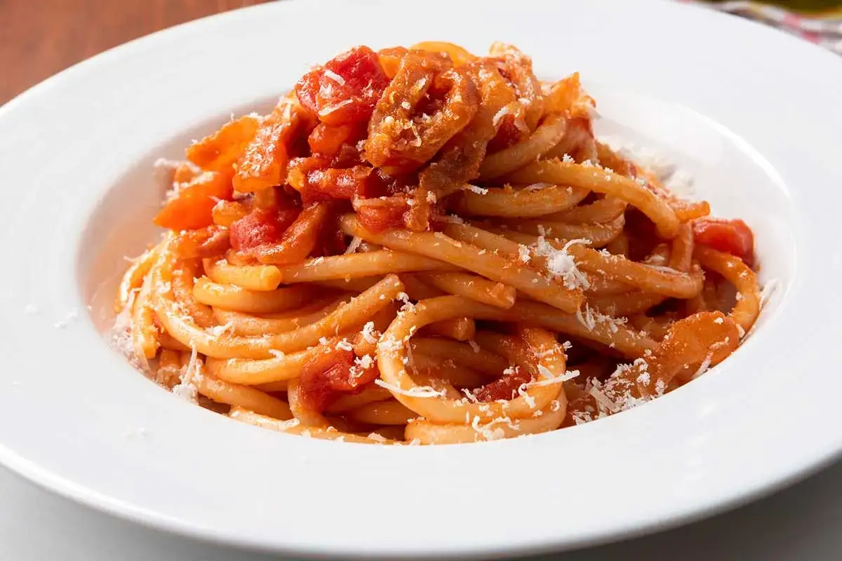 Un piatto invitante di bucatini all'amatriciana, conditi con sugo rosso e guanciale croccante, spolverati di pecorino.