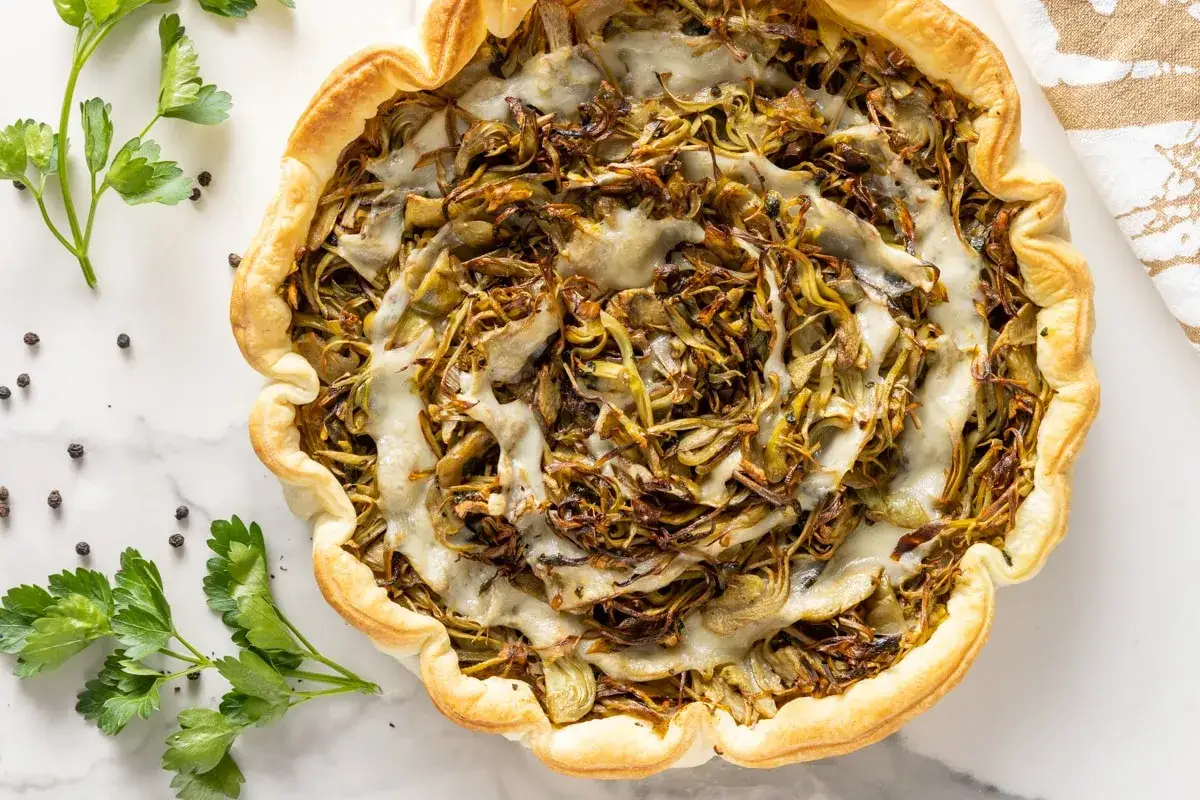 Torta salata con carciofi e ricotta al forno, dorata e invitante, guarnita con prezzemolo fresco e pepe nero.