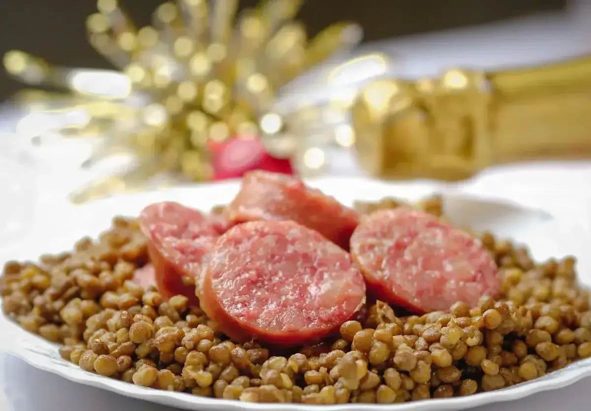 Lenticchie e cotechino, un classico della tradizione culinaria italiana, serviti su un piatto bianco con decorazioni natalizie sfocate sullo sfondo.