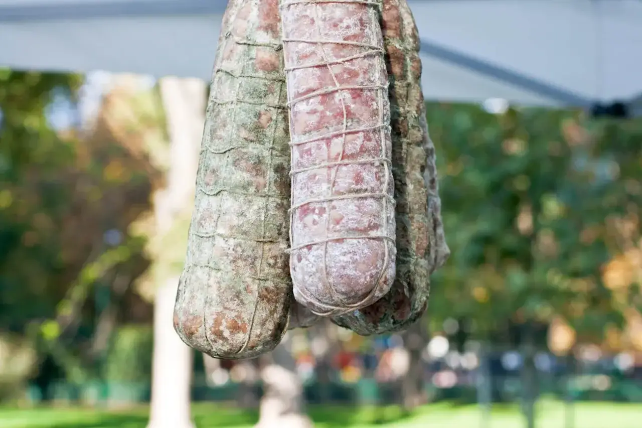 Tre salami appesi, con muffa bianca e verde, pronti per essere gustati. Un classico della carne insaccata.