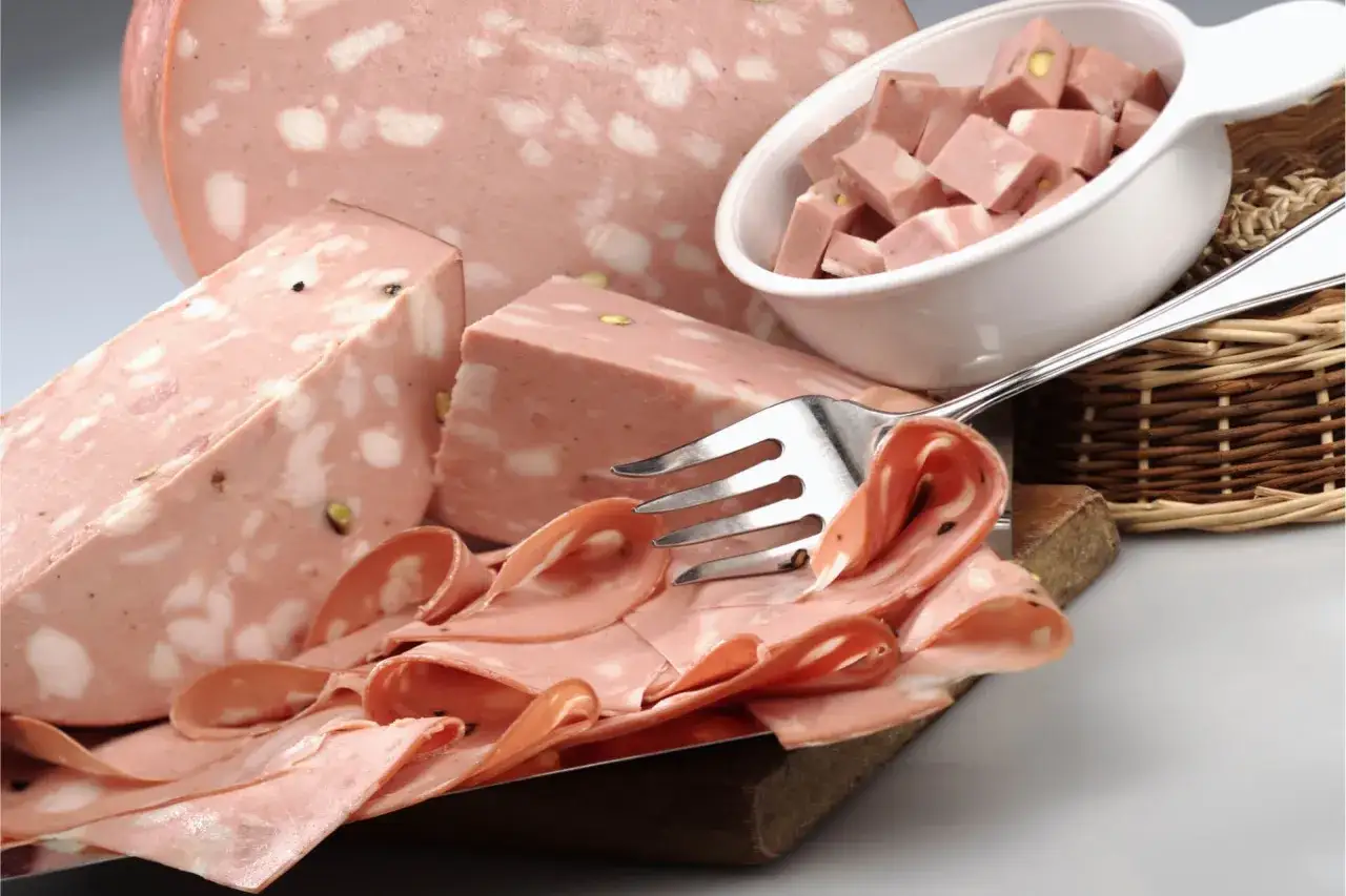 La mortadella, con i suoi cubetti e fette, mostra la differenza tra mortadella e bologna, con pistacchi e pepe visibili.