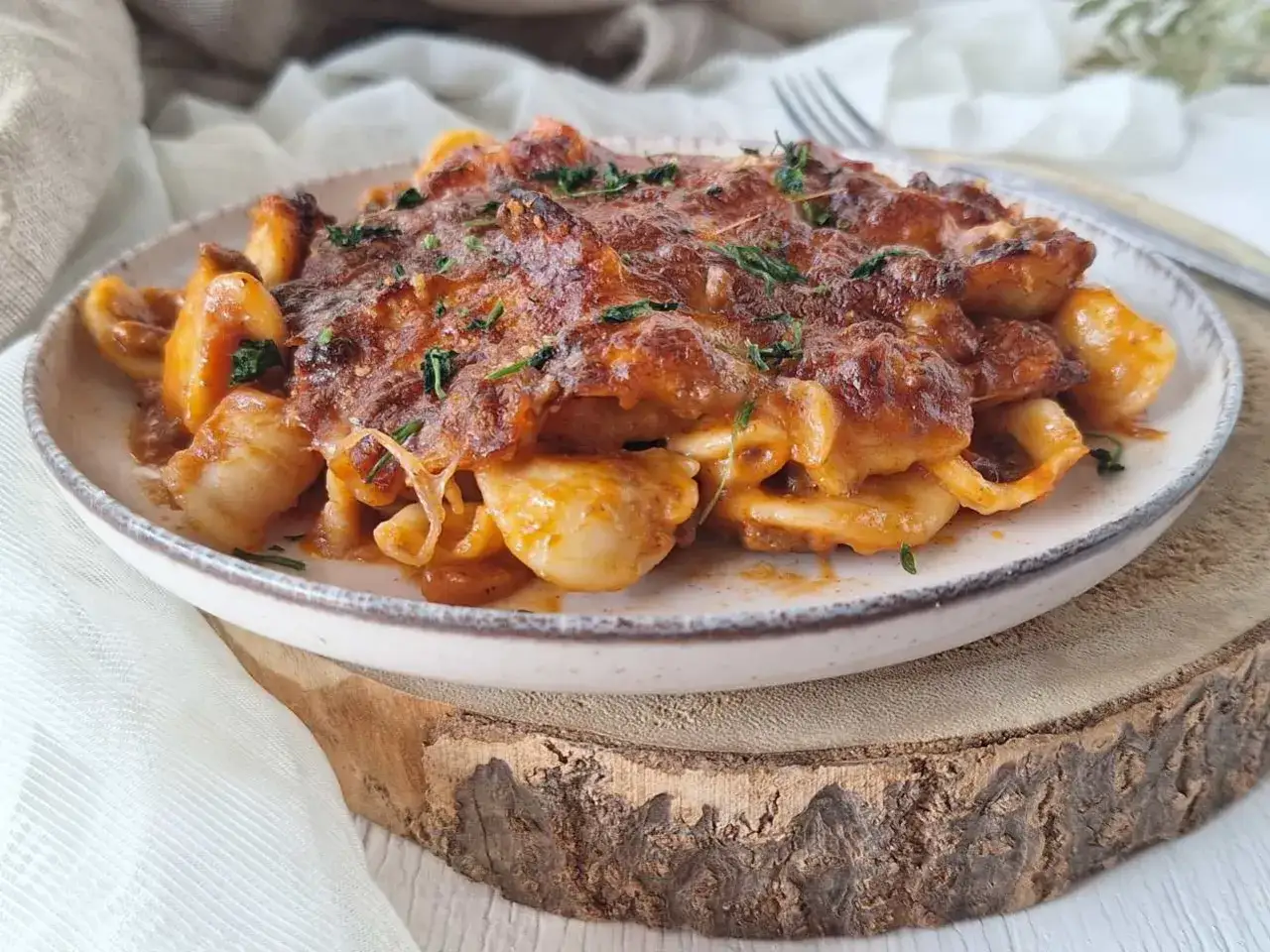 Piatto di pasta al forno con formaggio fuso e un filo di burro sciolto, guarnito con erbe aromatiche.