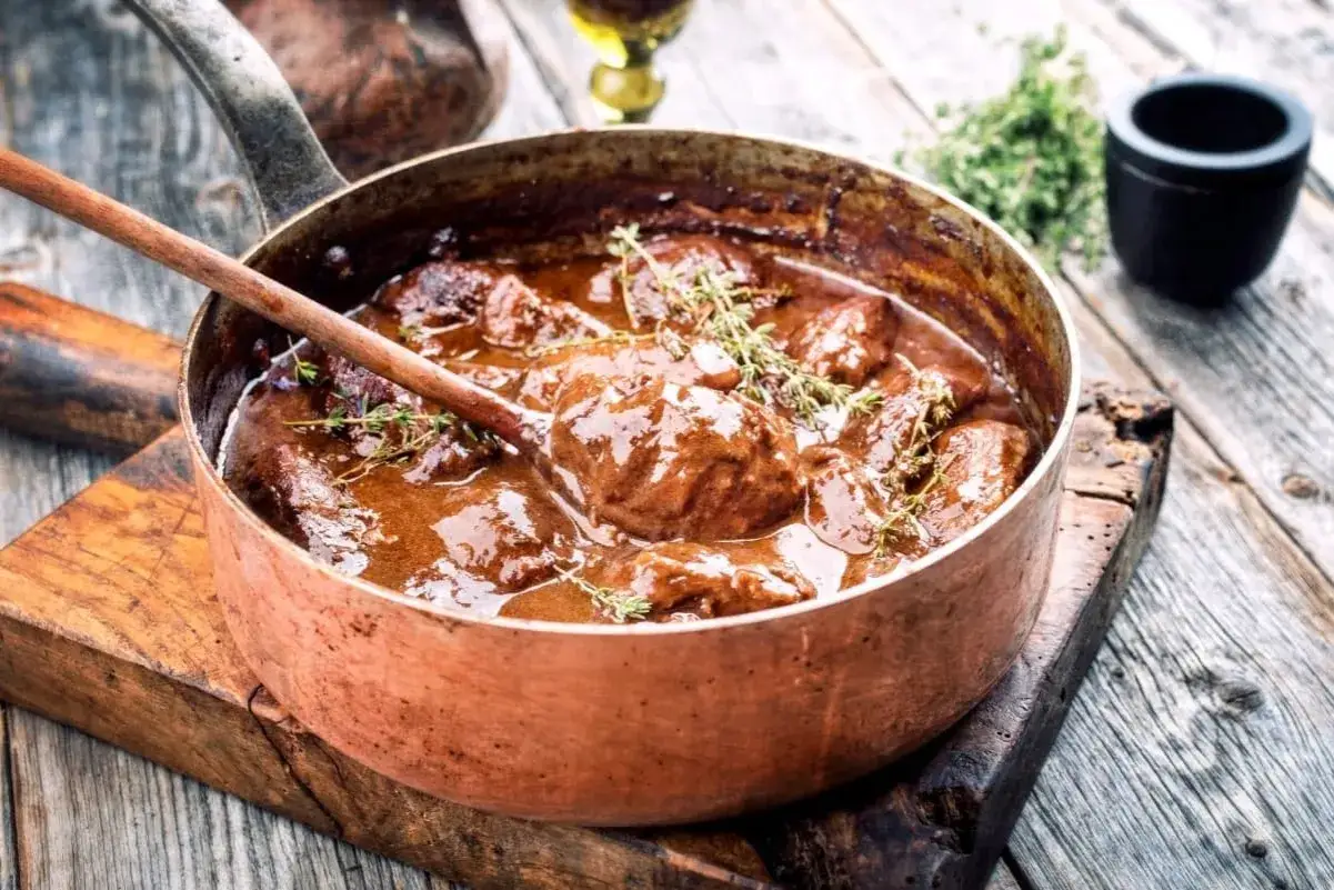 Brasato ricetta semplice in un tegame di rame, con rametti di timo fresco. Un piatto succulento pronto per essere gustato.