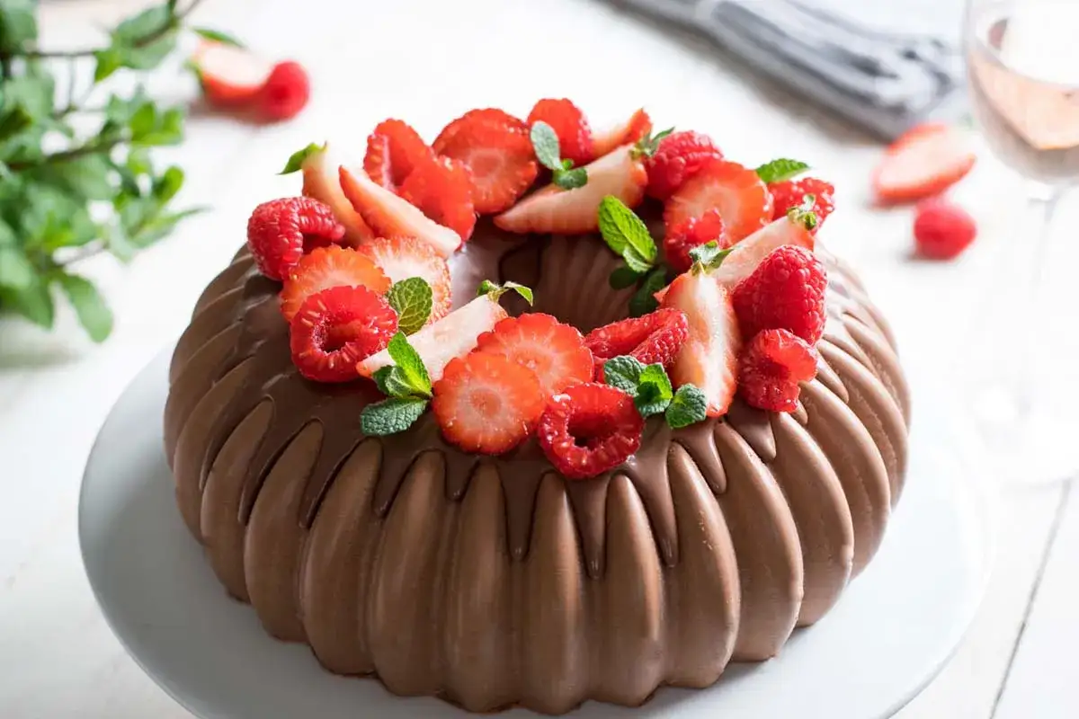 Torta mousse al cioccolato decorata con fragole, lamponi e menta fresca. Un dolce invitante e goloso.