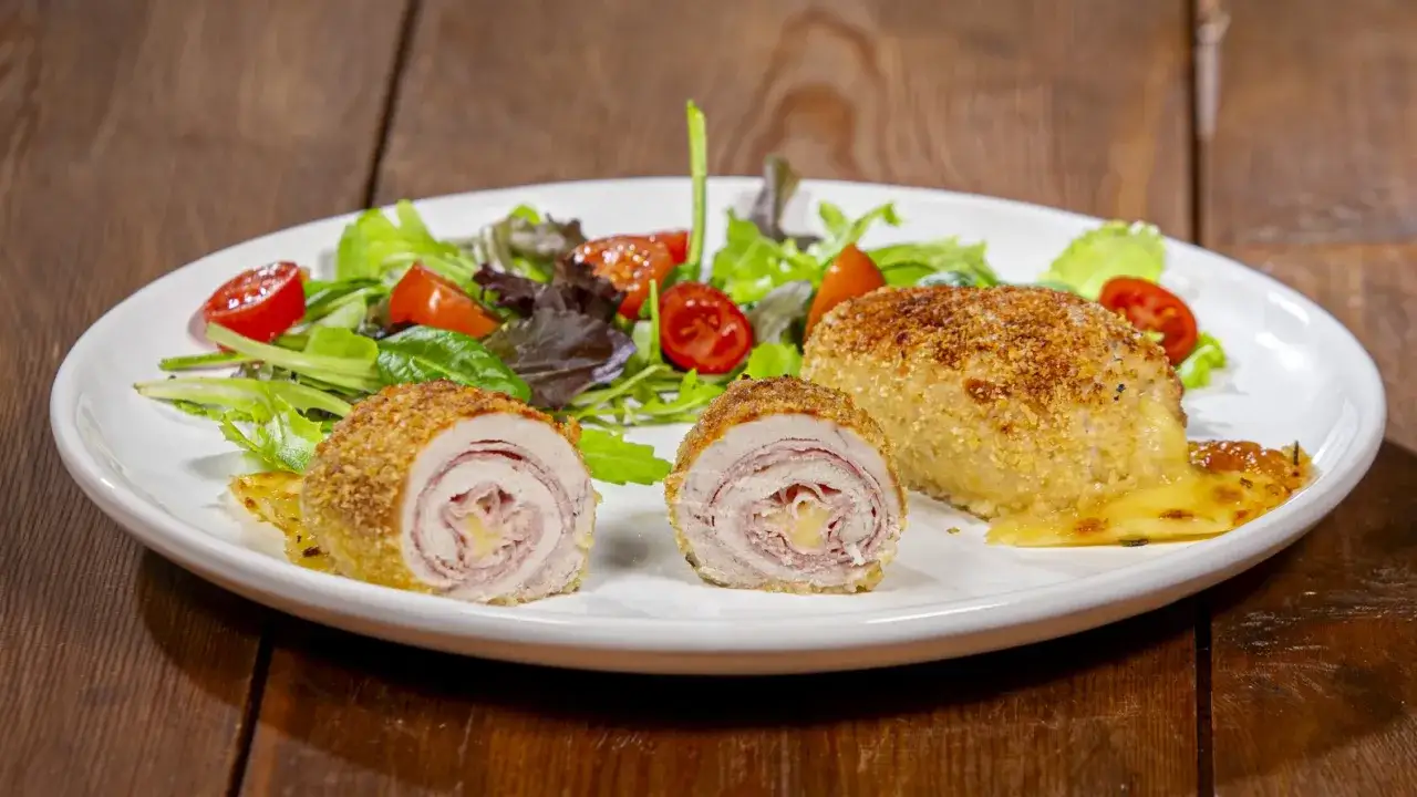 Involtini di pollo al forno croccanti, ripieni di prosciutto e formaggio filante, serviti con insalata fresca e pomodorini.