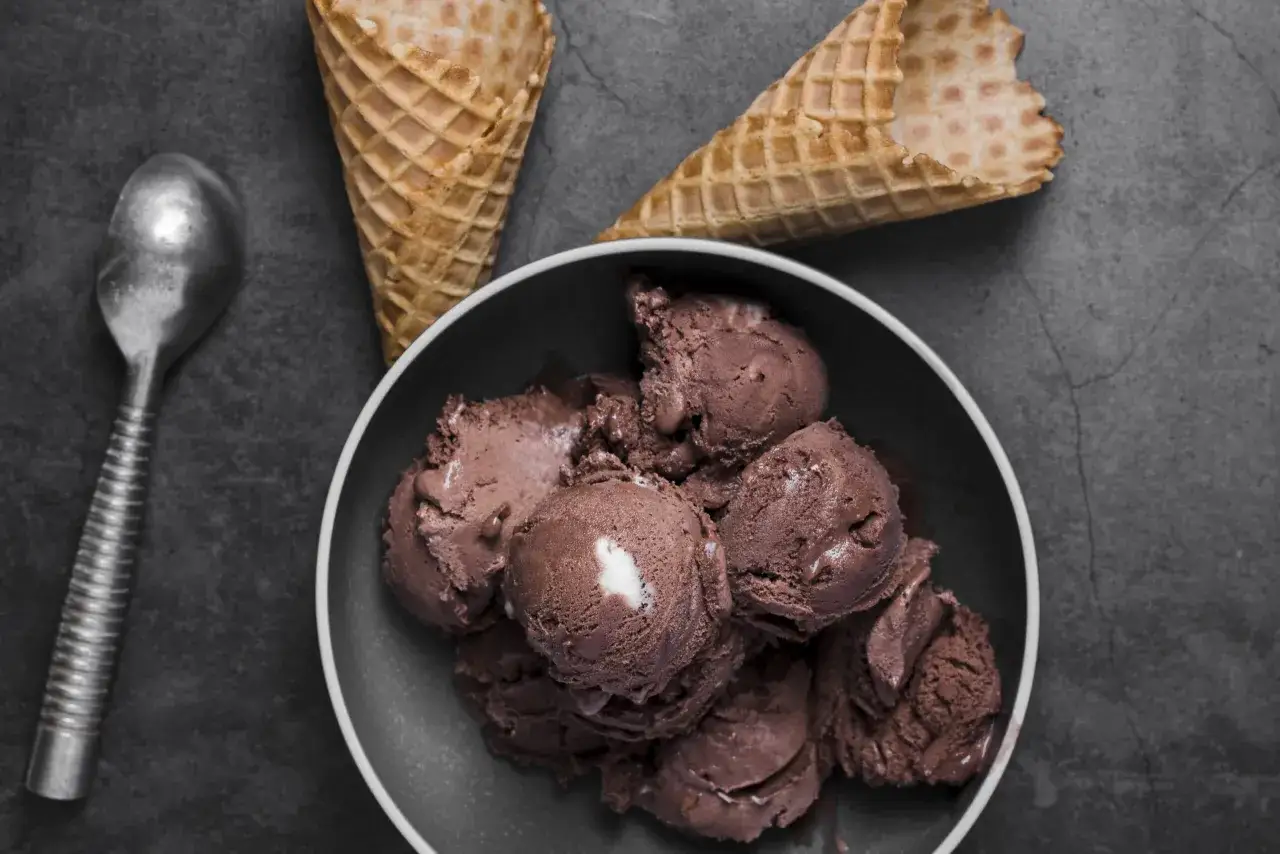Coppette di gelato al cioccolato, preparato senza gelatiera, pronte per essere gustate. Un cucchiaio d'argento e coni vuoti completano la scena.