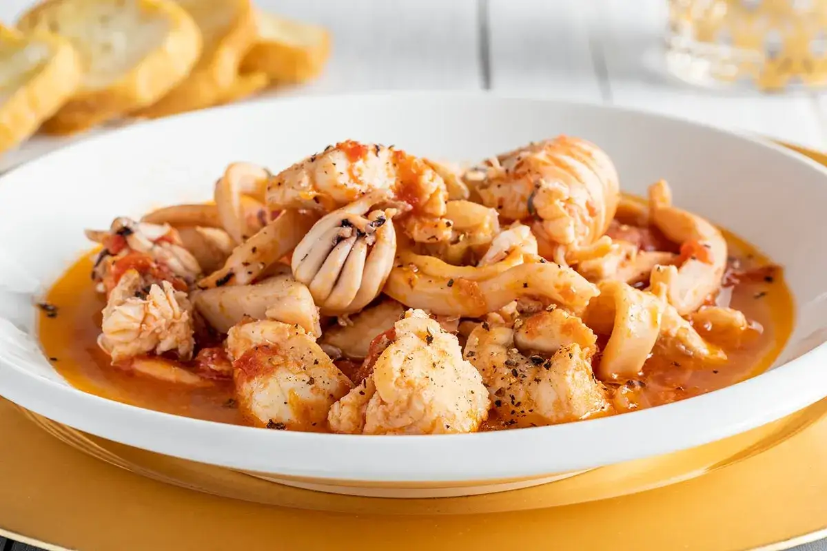 Un invitante piatto di zuppa di pesce, ricco di calamari e pesci misti, servito con pane tostato.