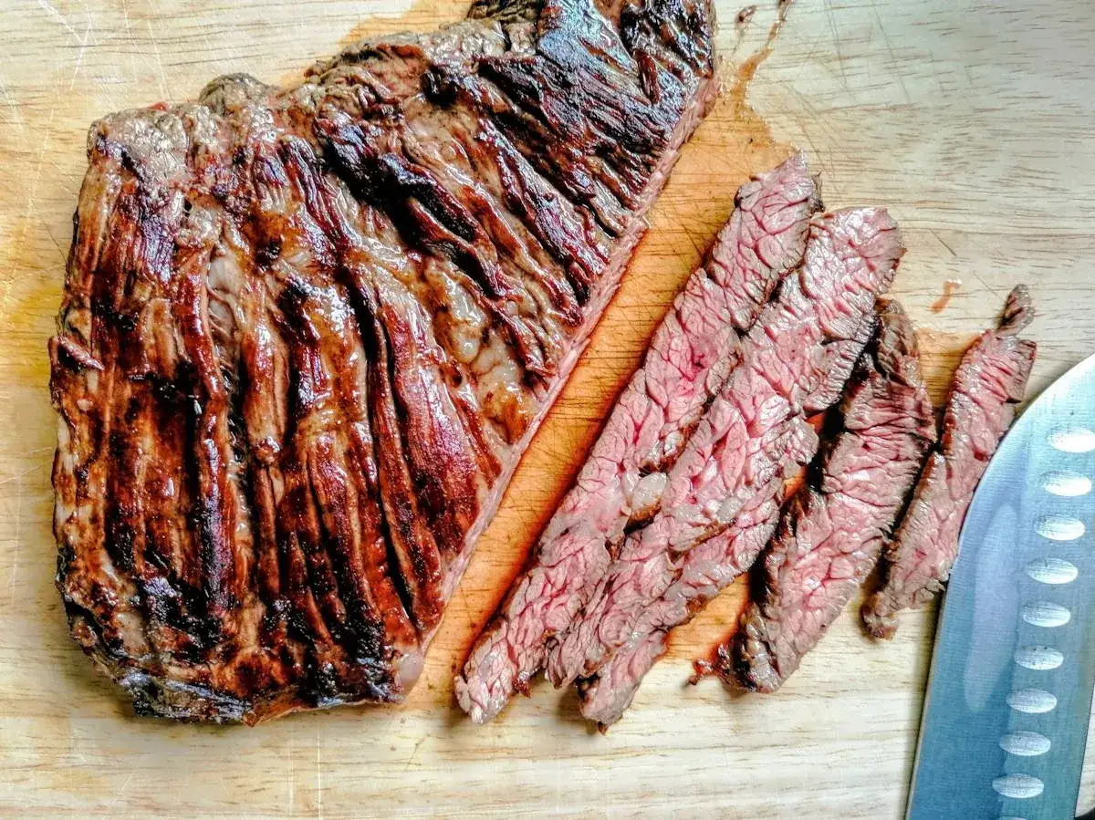 Succulento spider steak grigliato, affettato su tagliere di legno. La carne mostra striature rosse e una crosticina invitante.