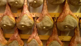 Filetti di salumi appesi a stagionare su scaffali di legno.