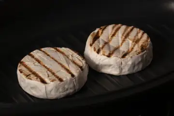 Due forme di formaggio da fare alla piastra, con belle striature dorate, cuociono in una padella scura.