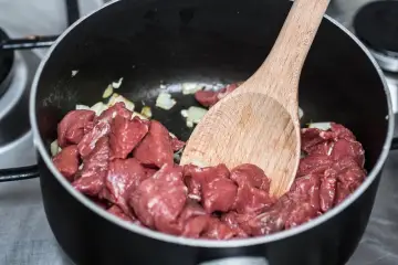 Bocconcini di manzo crudo in padella con cipolla, pronti per diventare uno spezzatino gommosa di manzo.