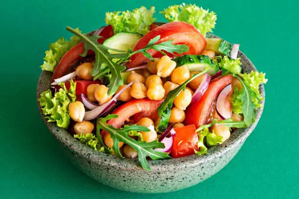 Insalata di ceci colorata con pomodori, cetrioli, cipolla rossa, lattuga e rucola in una ciotola grigia.