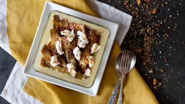 Carciofi e ricotta al forno in una teglia bianca, guarniti con pangrattato croccante. Serviti su un tovagliolo giallo.