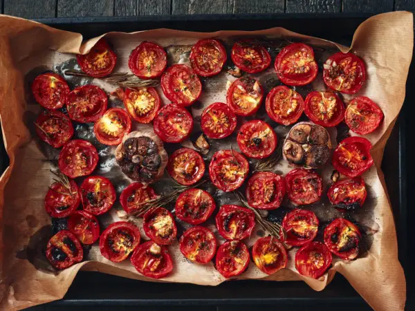 Pomodori al forno, caramellati e succosi, con aglio arrostito e rosmarino su carta forno.