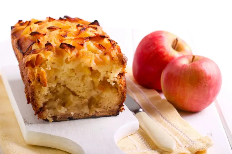 Torta con pandoro avanzato e mele, dorata e profumata, accanto a mele rosse fresche.