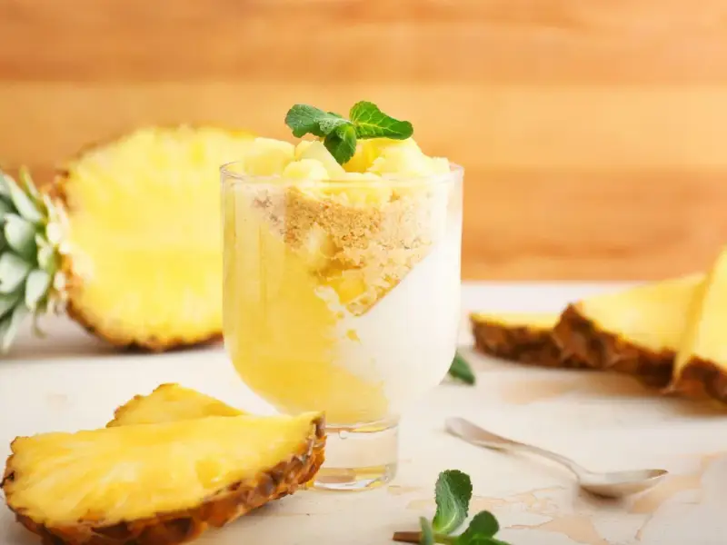 Delizioso dolce con ananas fresco, yogurt e crumble. Un bicchiere pieno di gusto tropicale, con fette di ananas e menta a guarnire.