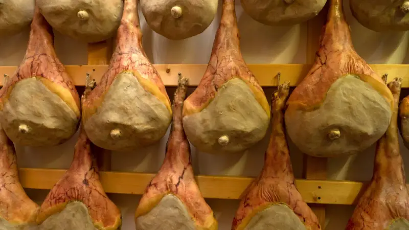 Filetti di salumi appesi a stagionare su scaffali di legno.