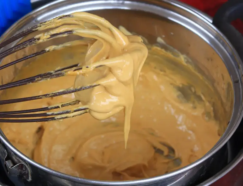 Una frusta raccoglie una crema densa e dorata, pronta per diventare uno zabaione freddo.